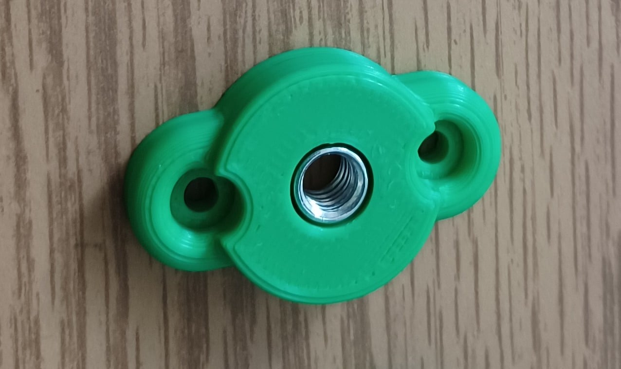 Green 3d printed light touch button with a t-nut inserted on a wood background.