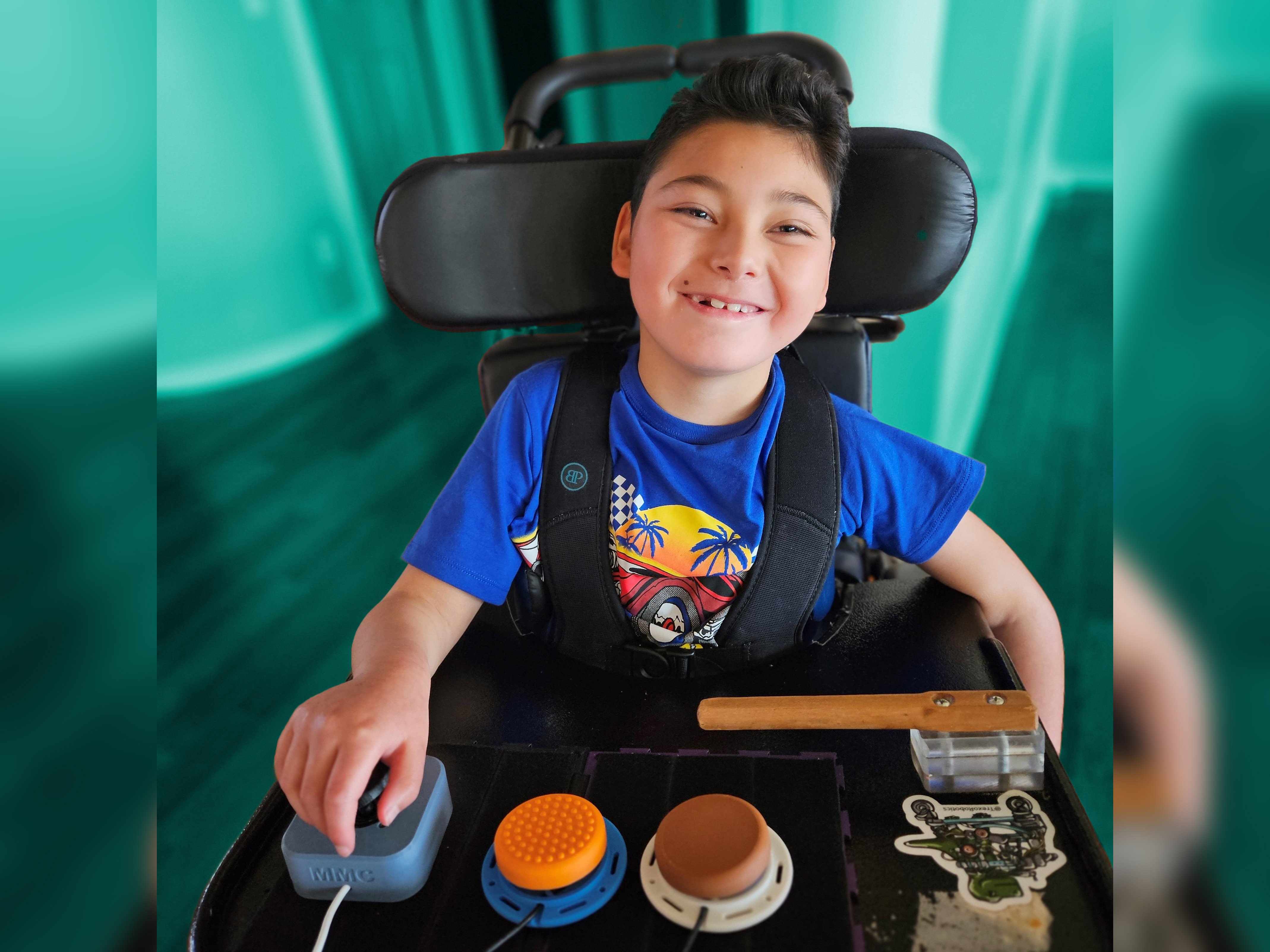 A young boy in a wheelchair with a 3d printed joystick and 2 switches in front