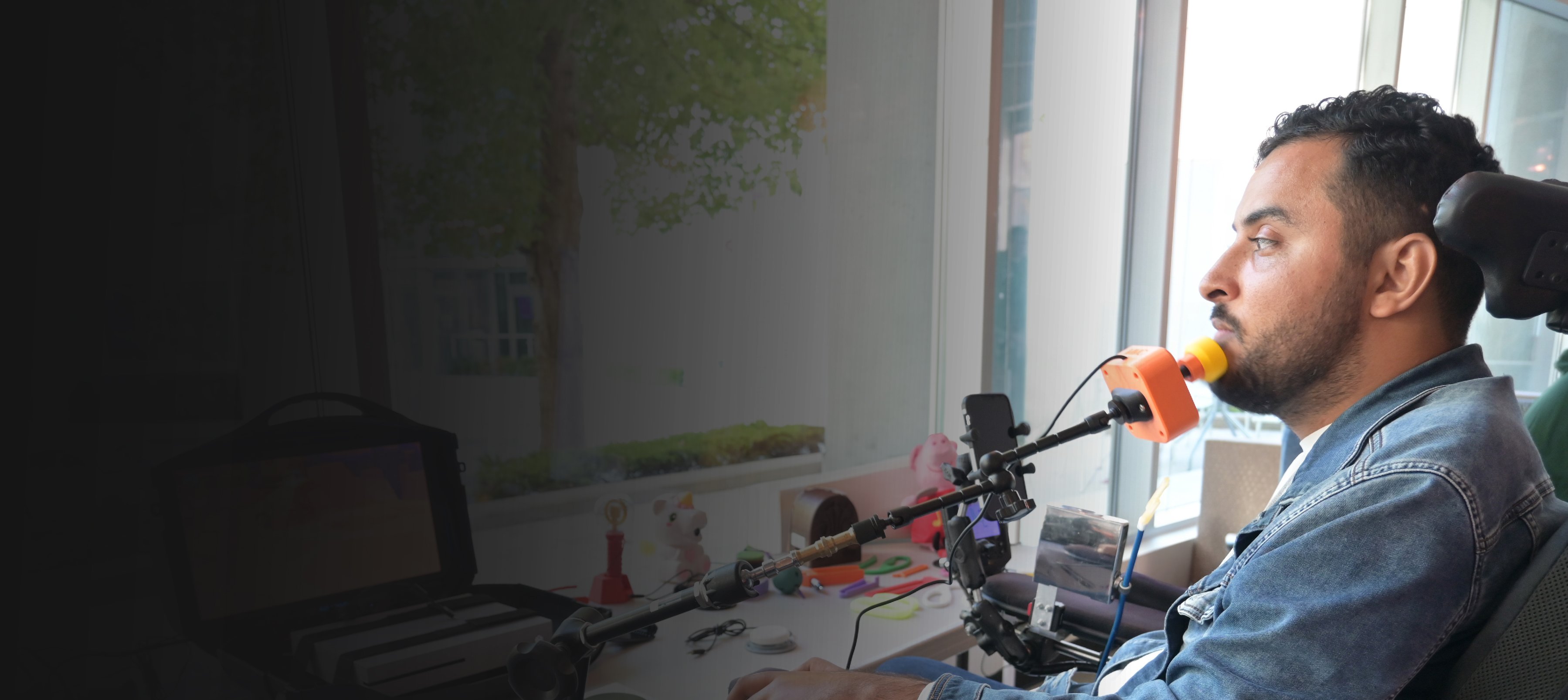 A man in a wheelchair using a 3D printed joystick to play a video game.