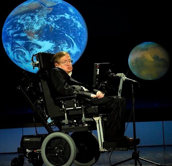 Stephen Hawking pictured in front of a screen featuring planets.