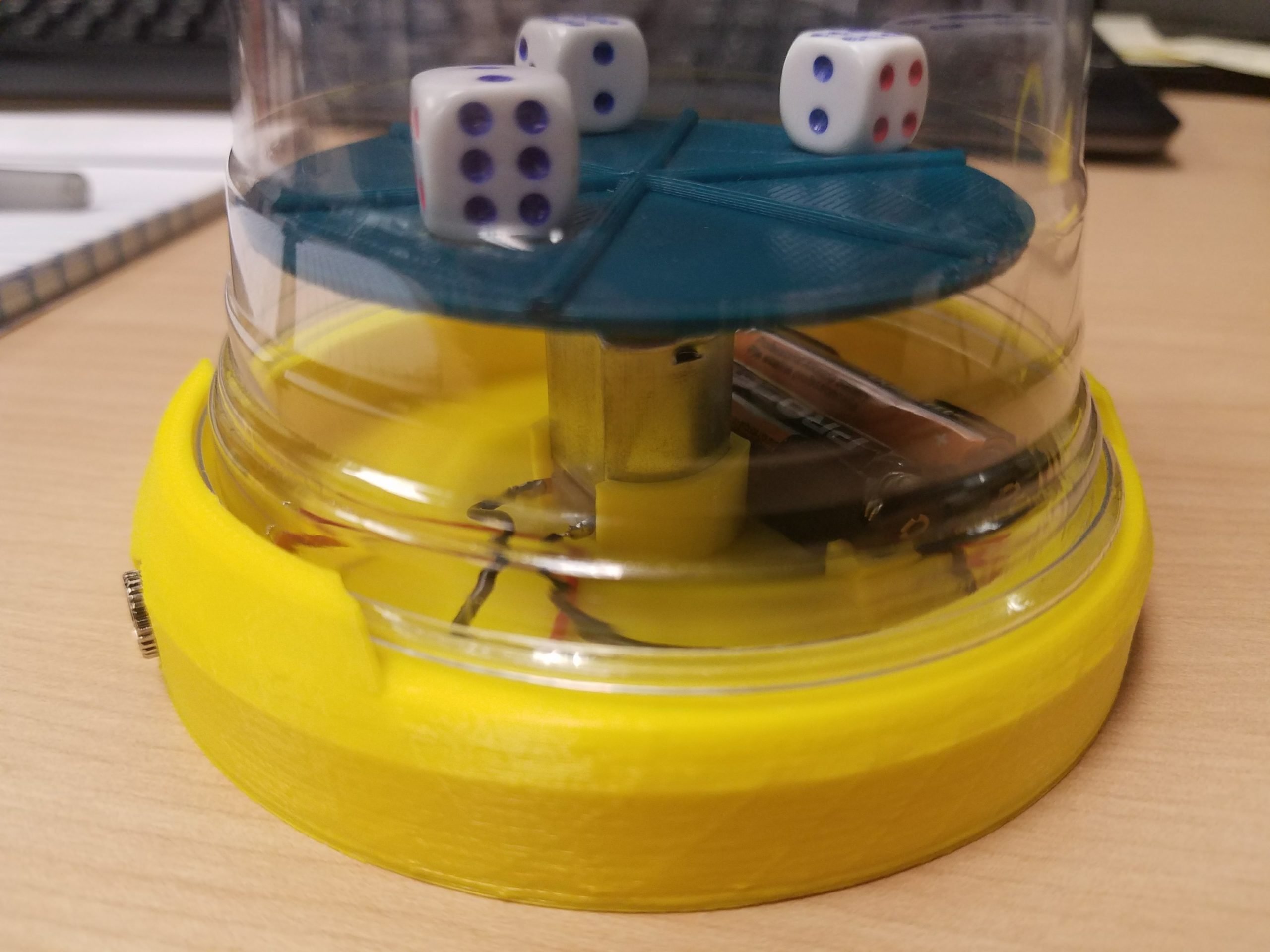 A yellow and green 3d printed dice spinner iwth three dice on a spinning plate.