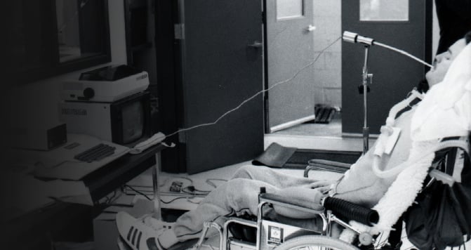 A black and white photo of Neil Squire in a wheelchair using a sip-and-puff device to type Morse Code.