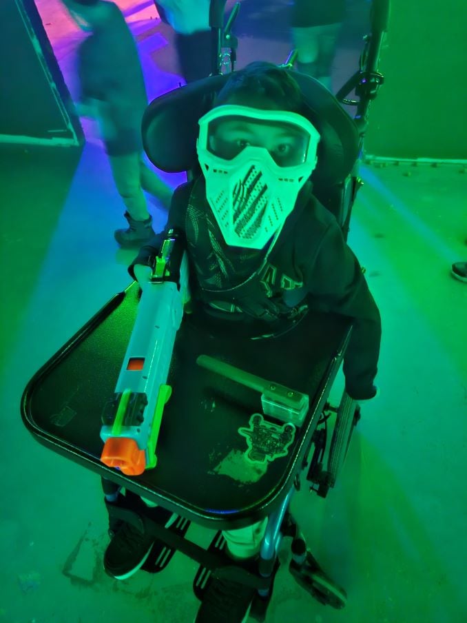 Adam in his wheelchair in a neon-lit nerf facility with a switch-adapted nerf gun.