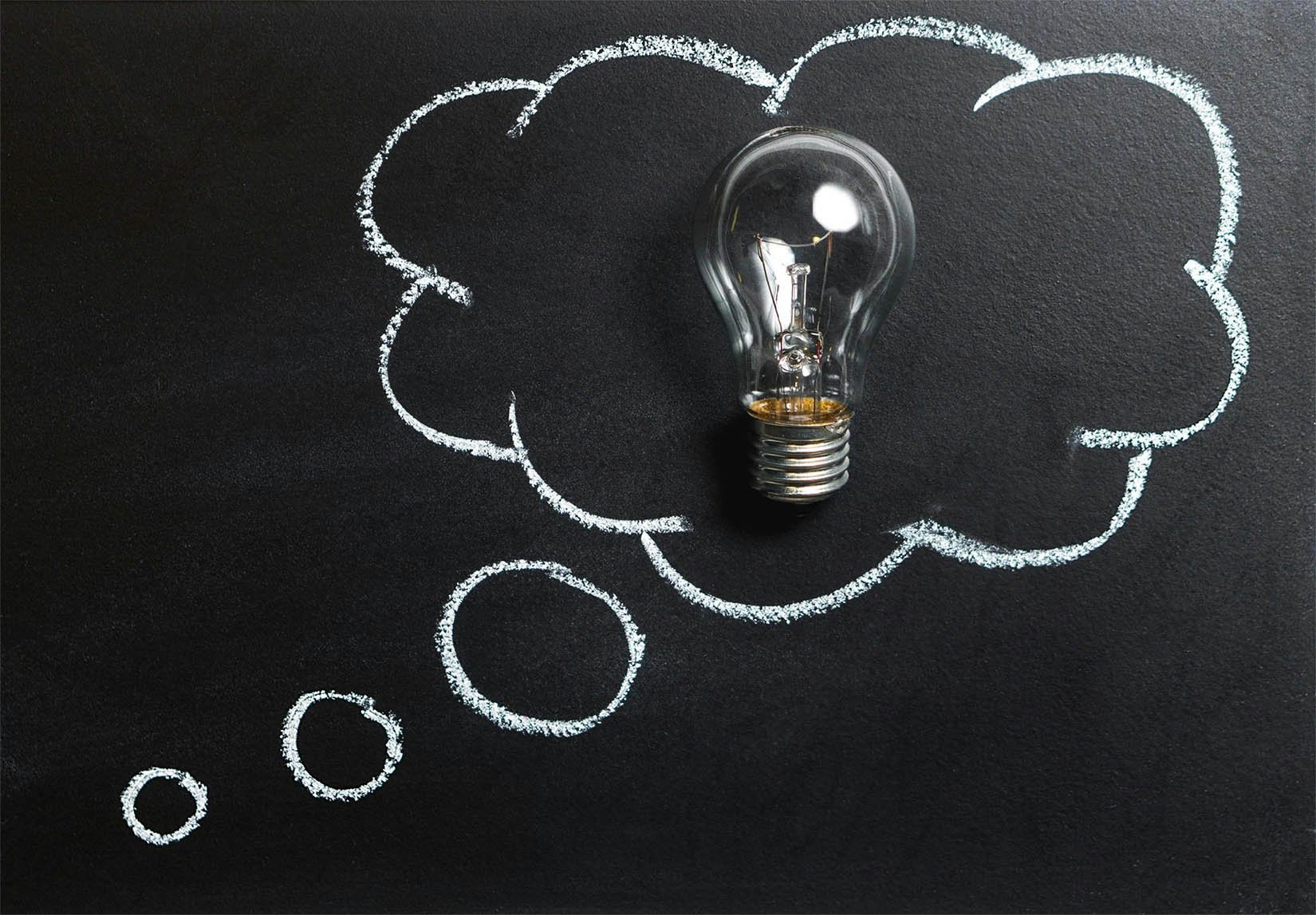 A light bulb on a black chalkboard with a line drawing of a thought bubble around it