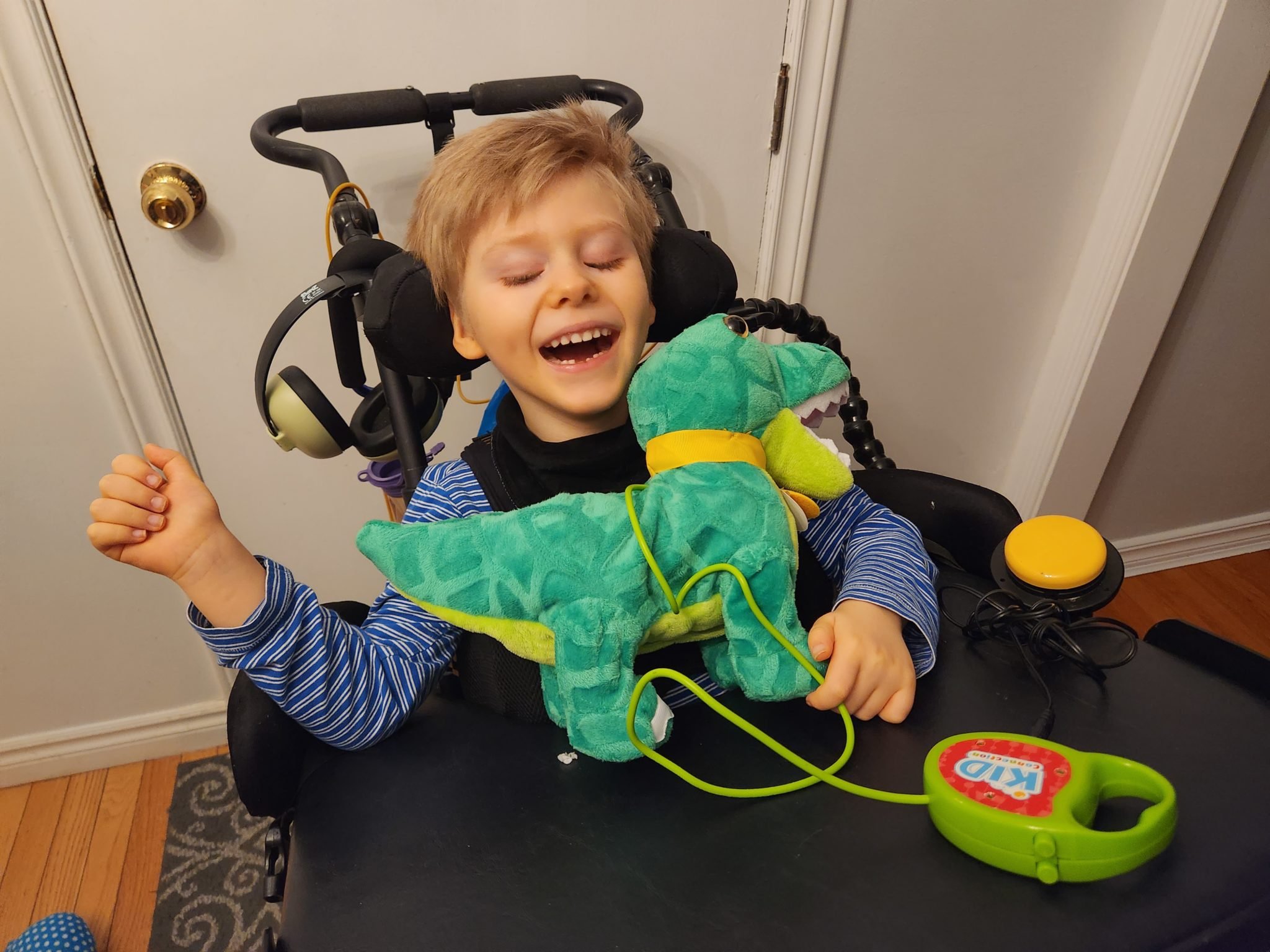 Chester in a black wheelchair and smiling at his green dino adapted toy.