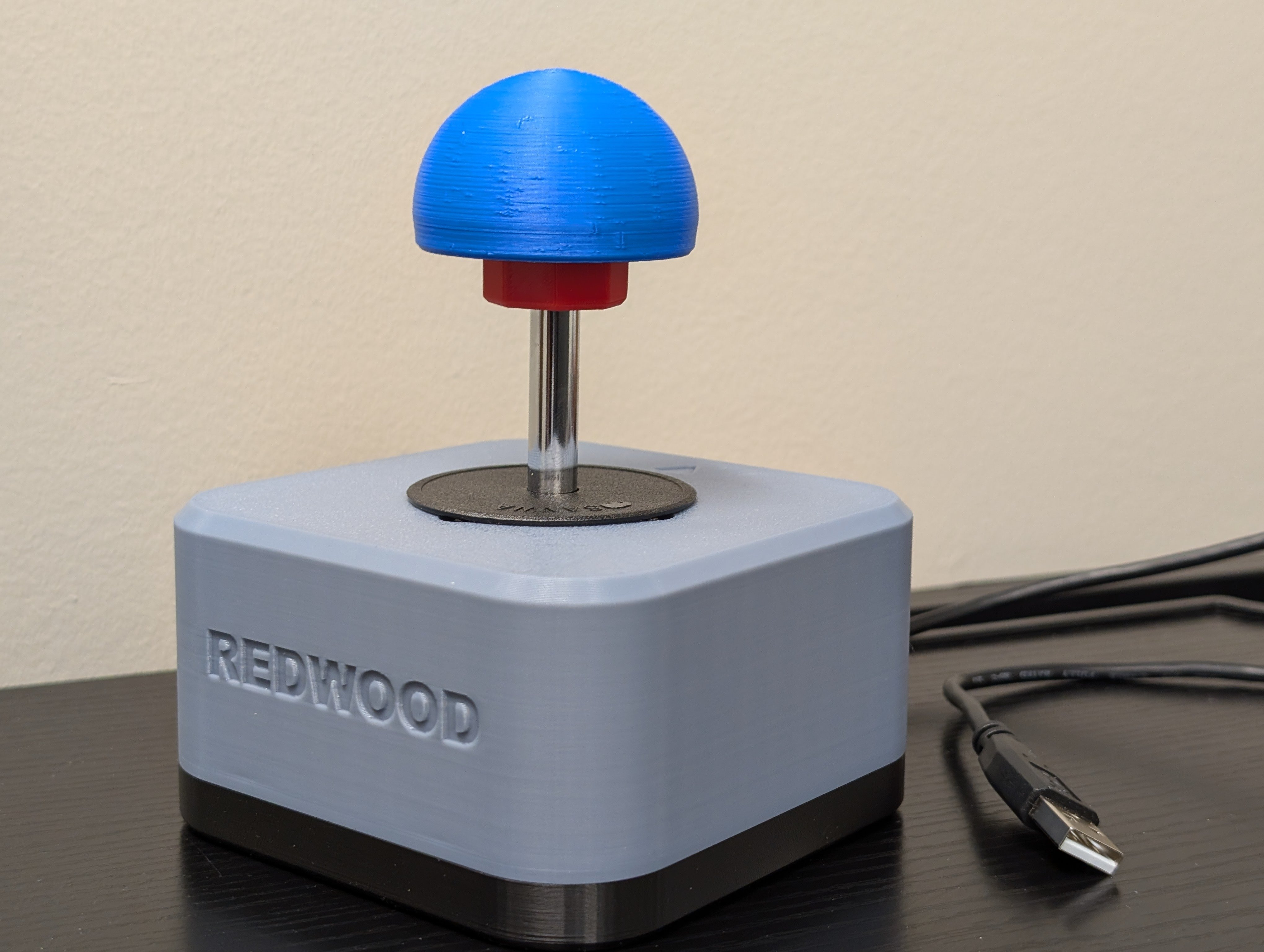 Isometric view of the Redwood joystick with 3D printed ball topper. A USB type A cable can be seen on the side. Top enclosure is light blue and base is black.