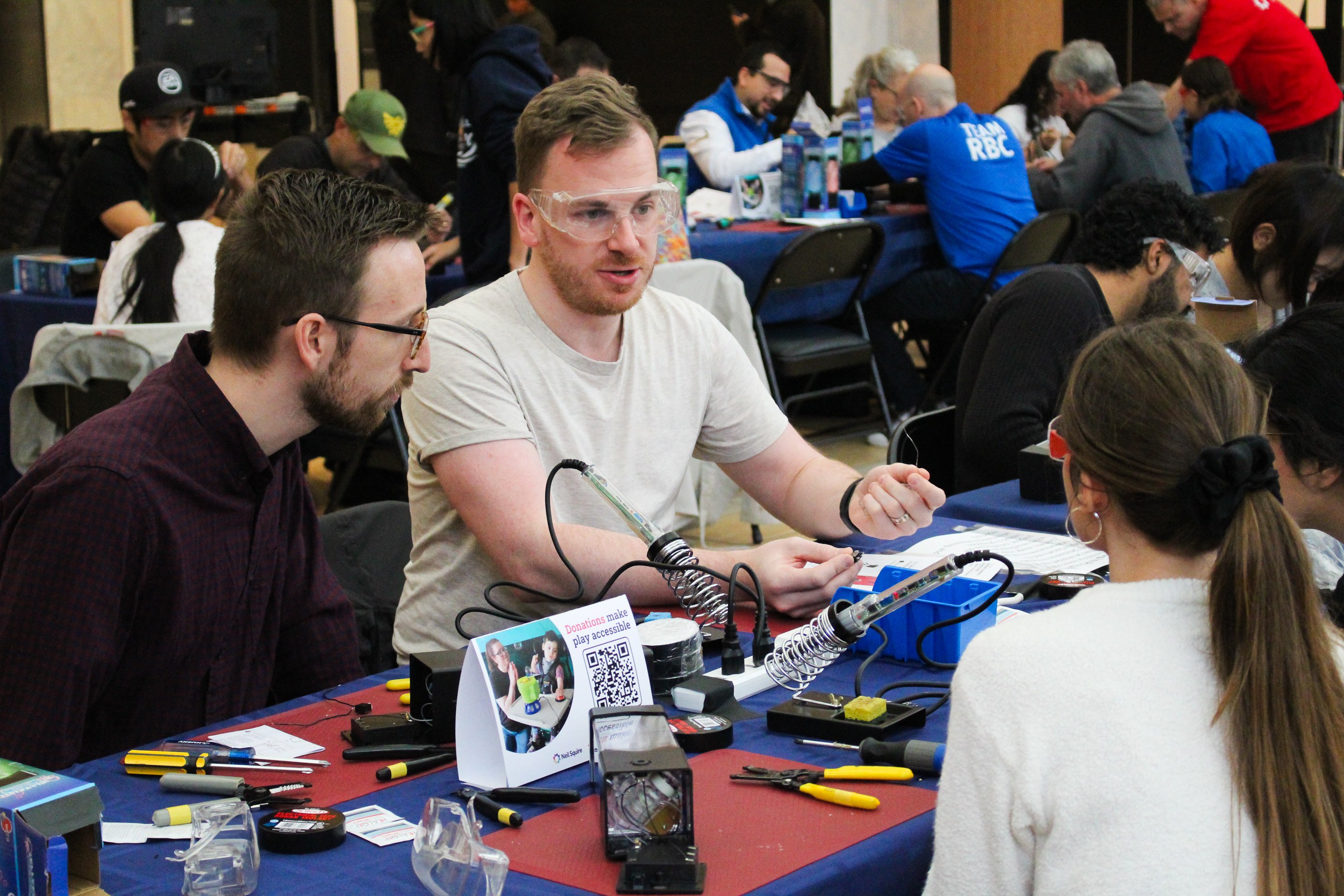 A man wearing safety talks with his fellow toy hackers.