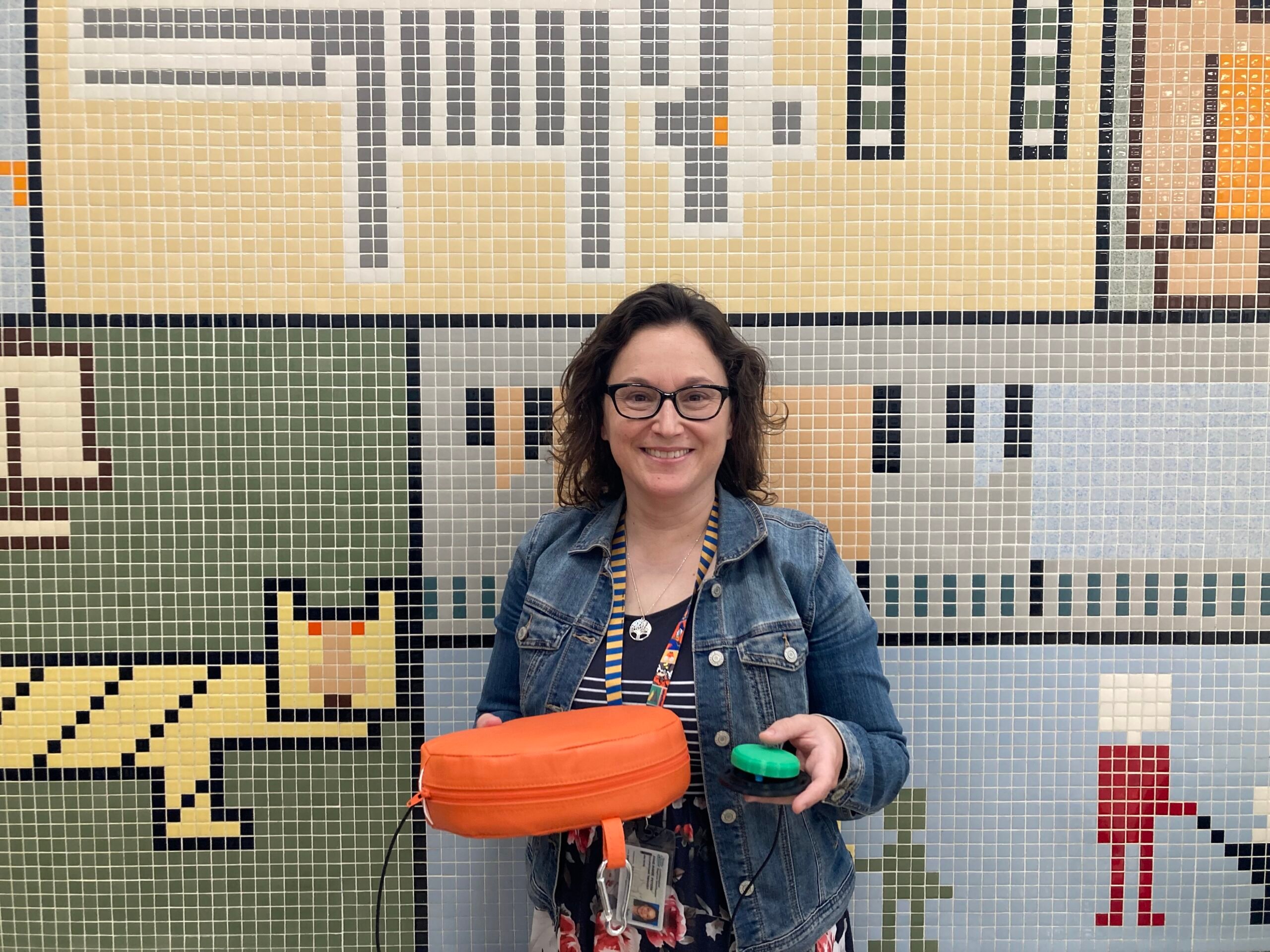 An occupational therapist with wavy brown hair holding an adapted vibrating cushion and switch