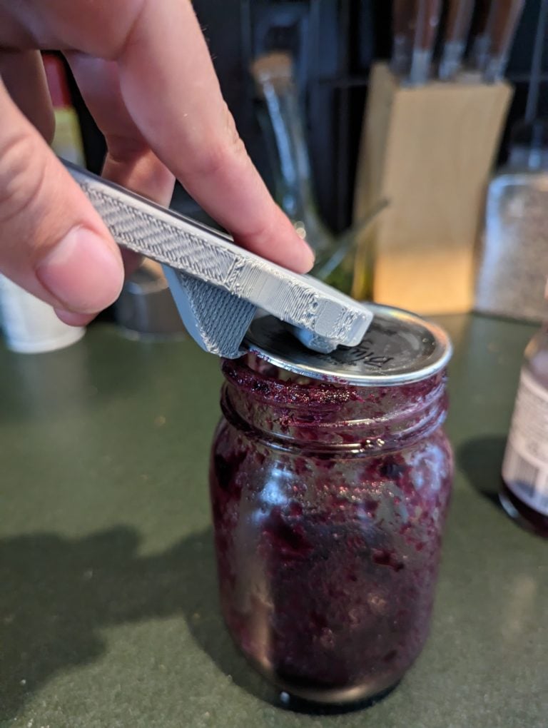 A grey jar lid opener being used to open a jar lid.