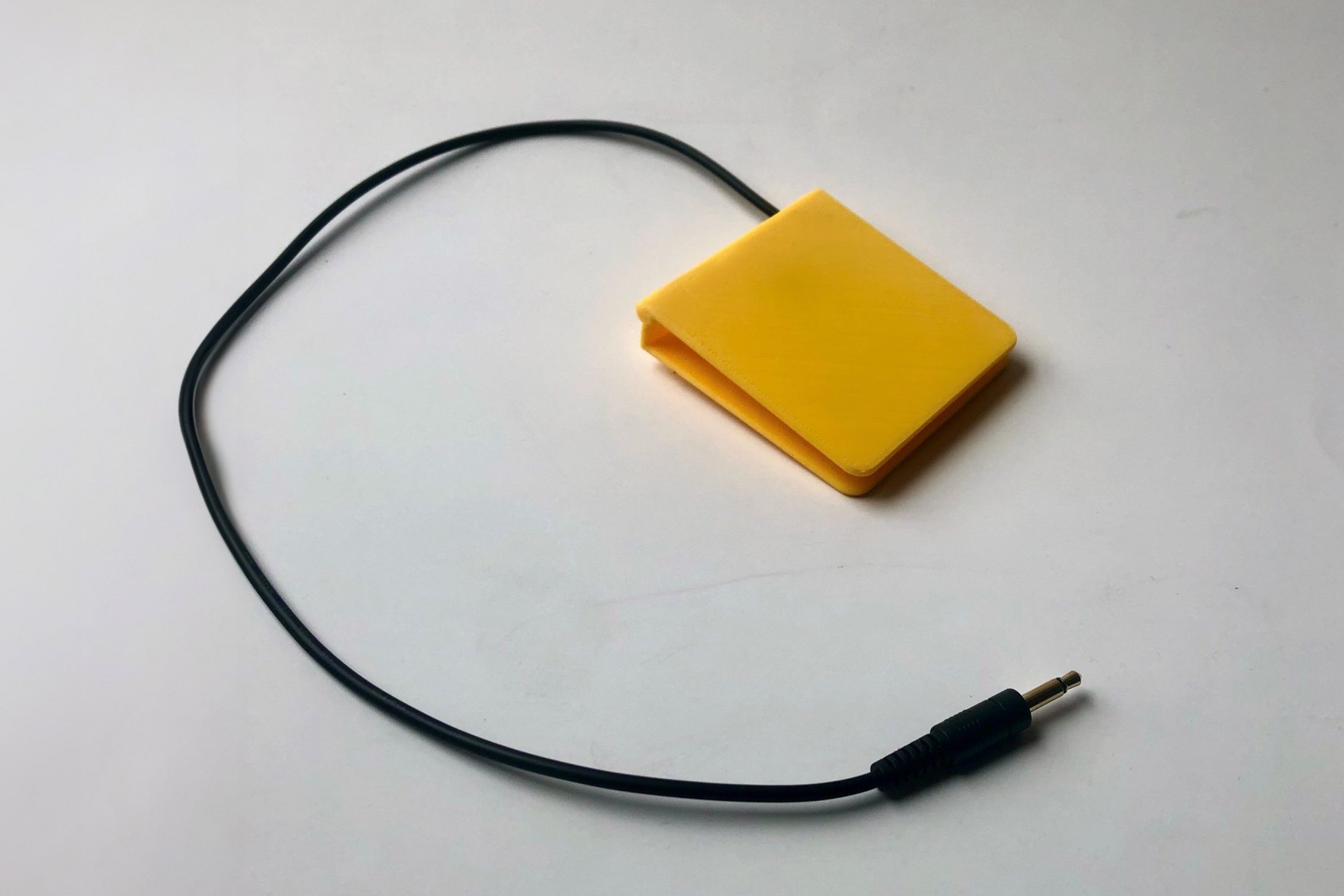 A yellow 3d printed low profile assistive switch with a mono jack end.