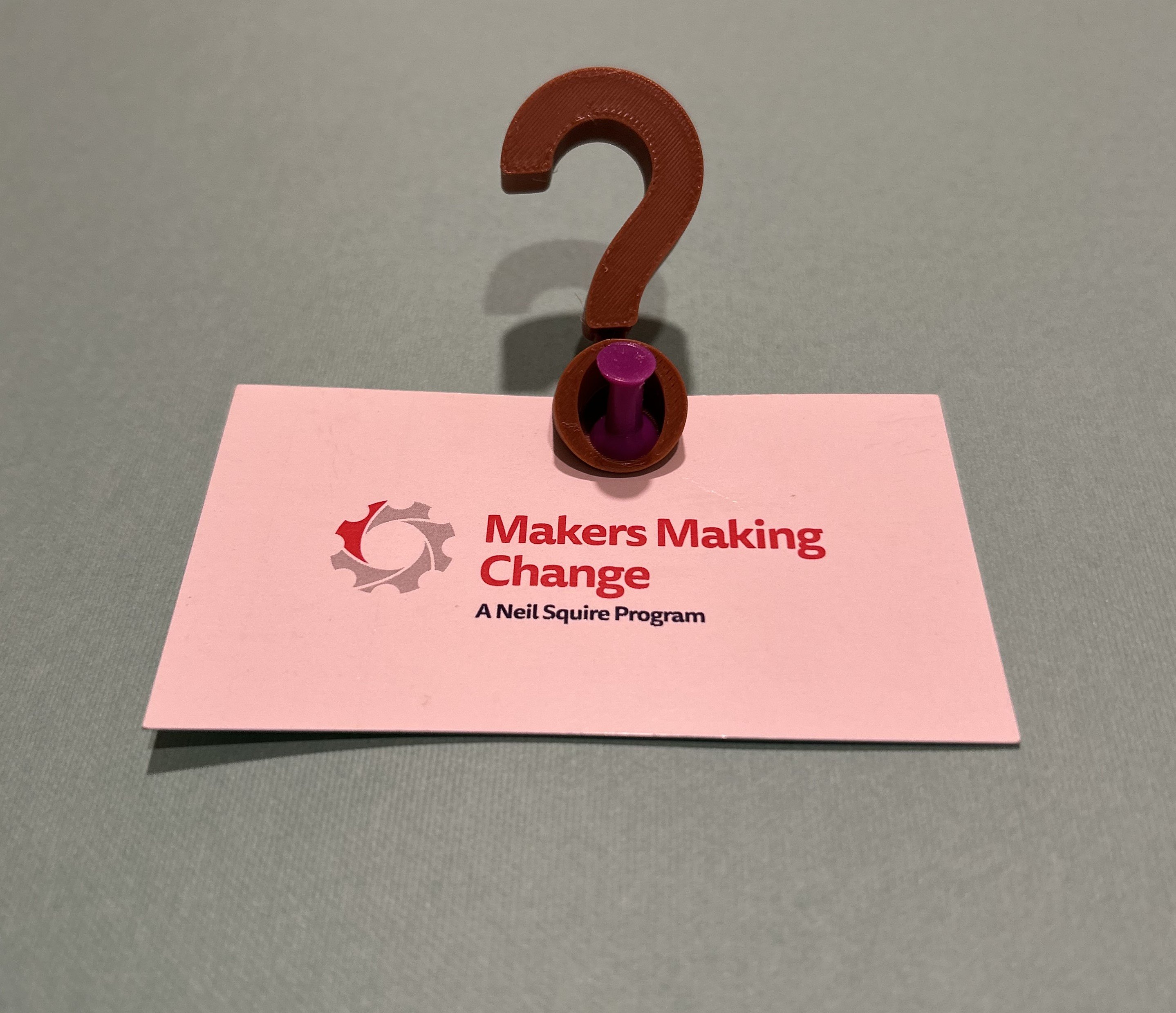 A 3d printed questions mark holding an MMC business card.