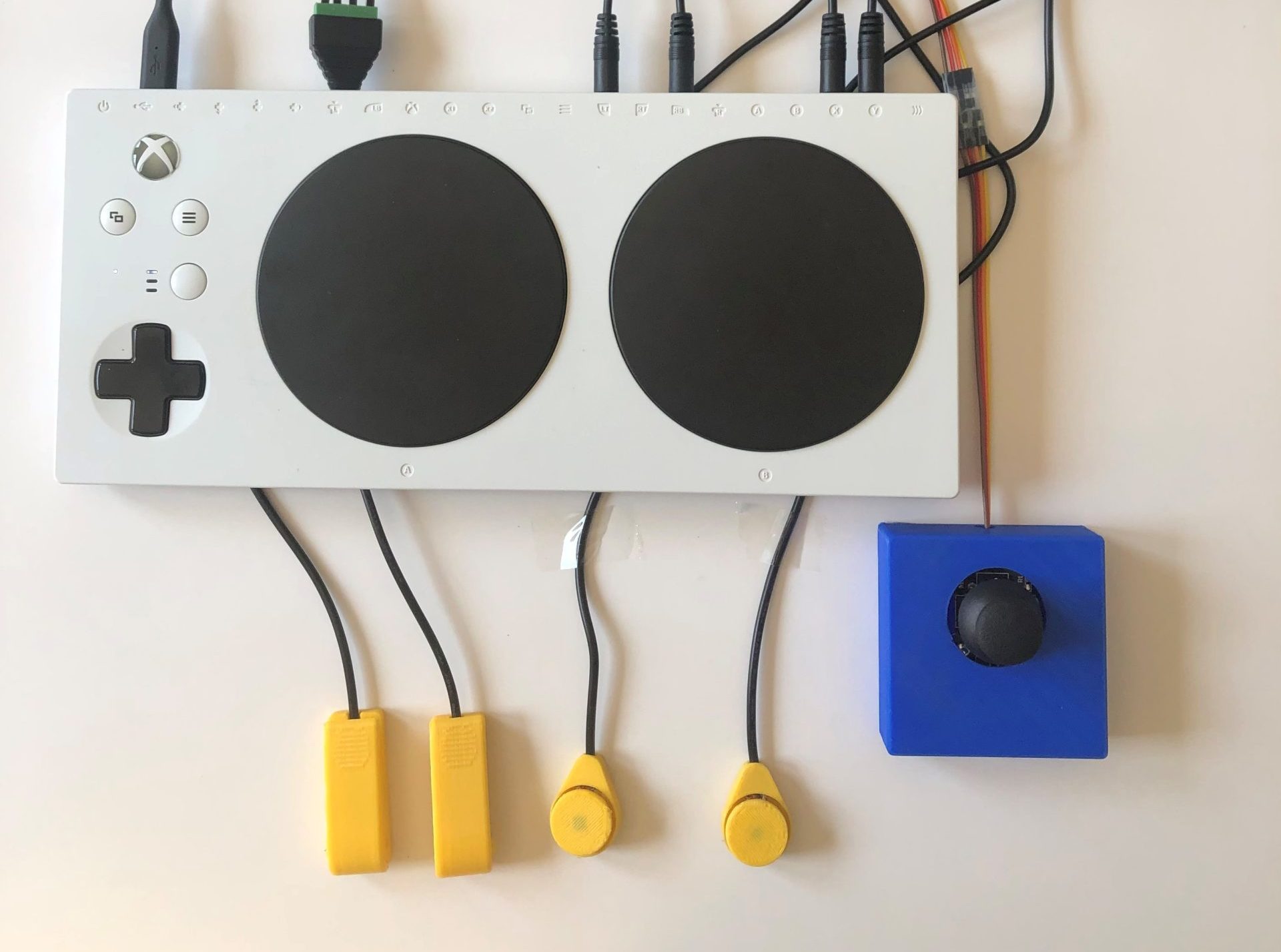A blue 3d printed analog thumbstick and 4 yellow assistive switches plugged into the Xbox Adaptive Controller.
