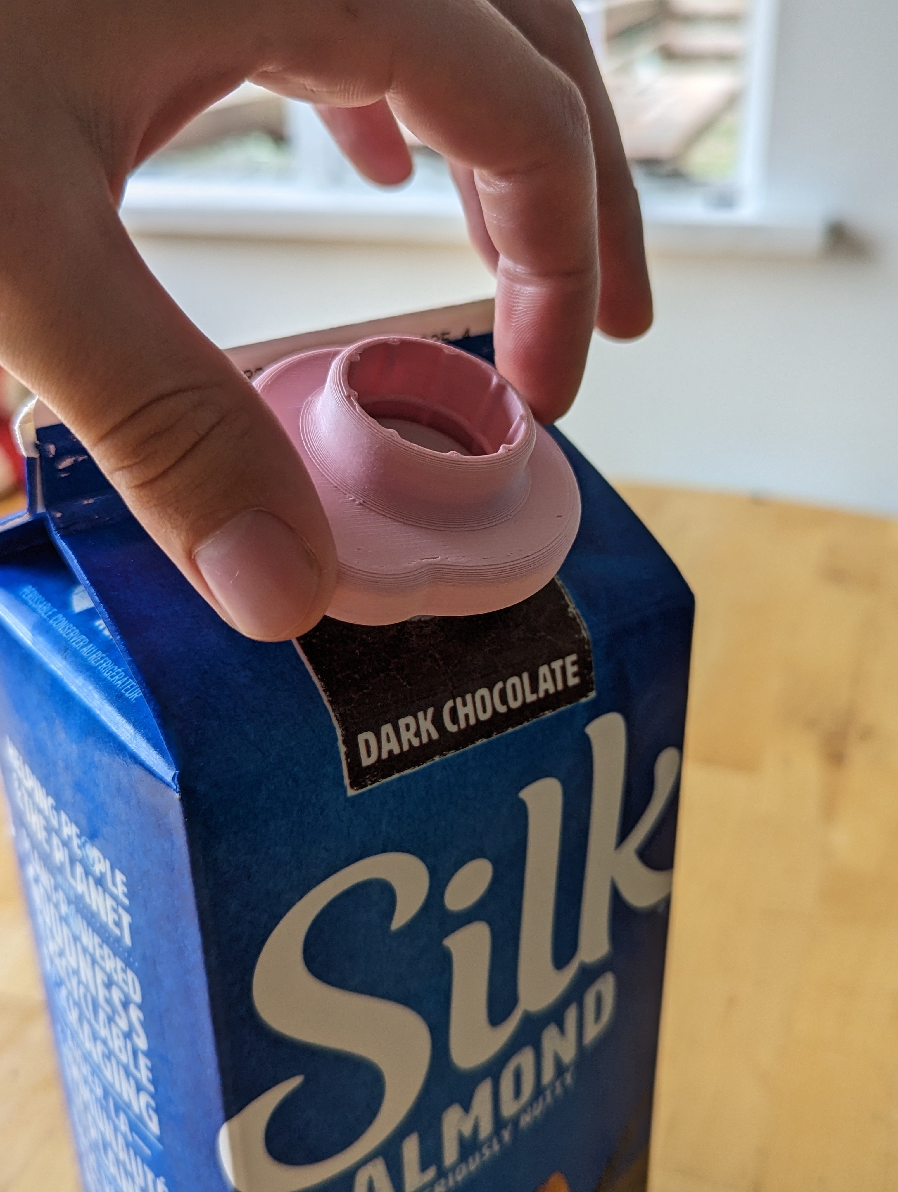 Person holding the milk carton opener over the twist off lid of a tetra pak beverage container