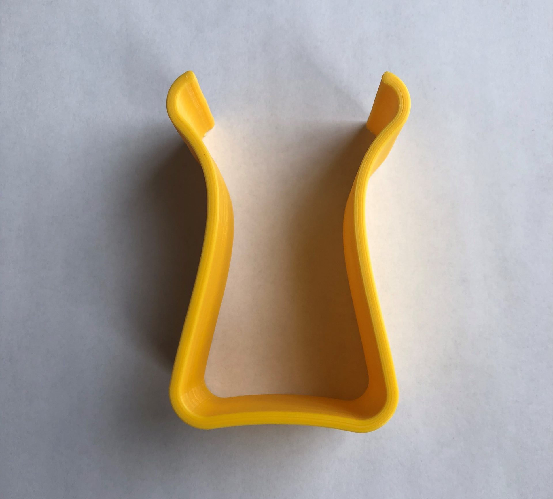 A yellow 3d printed u-shaped magnification stand against a white background.