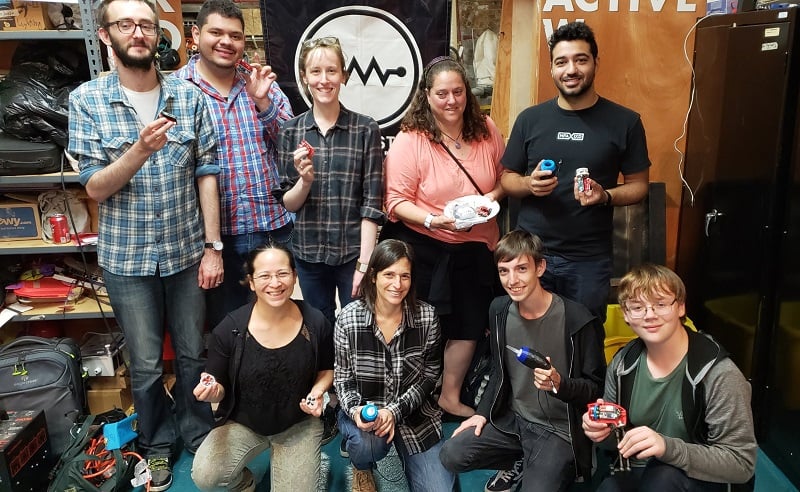 Nine makers at NYC Resistor holding their built devices.
