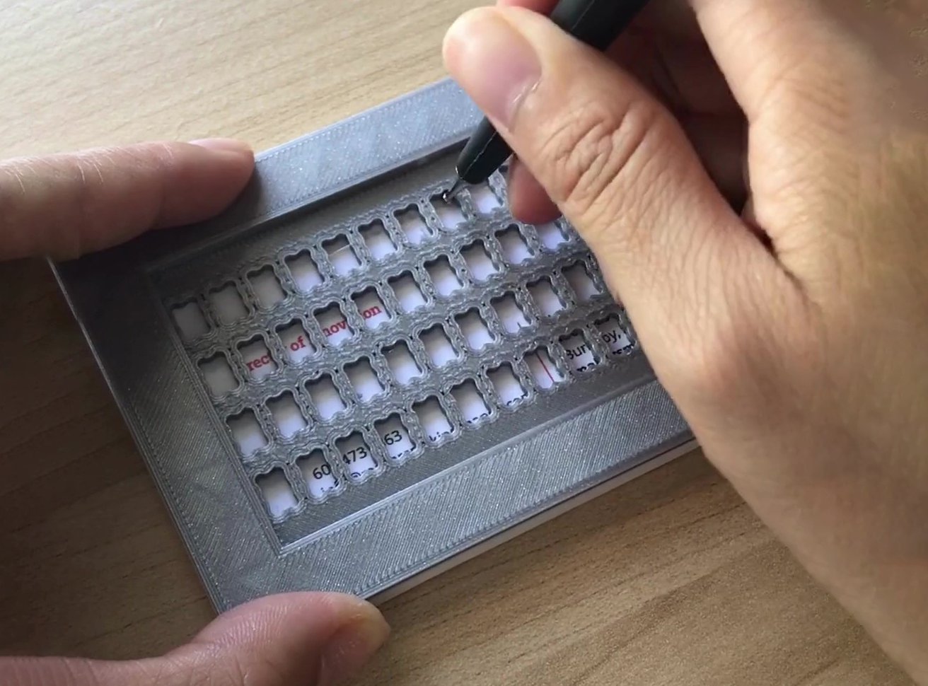 A hand embossing braille on a business card using the stylus set