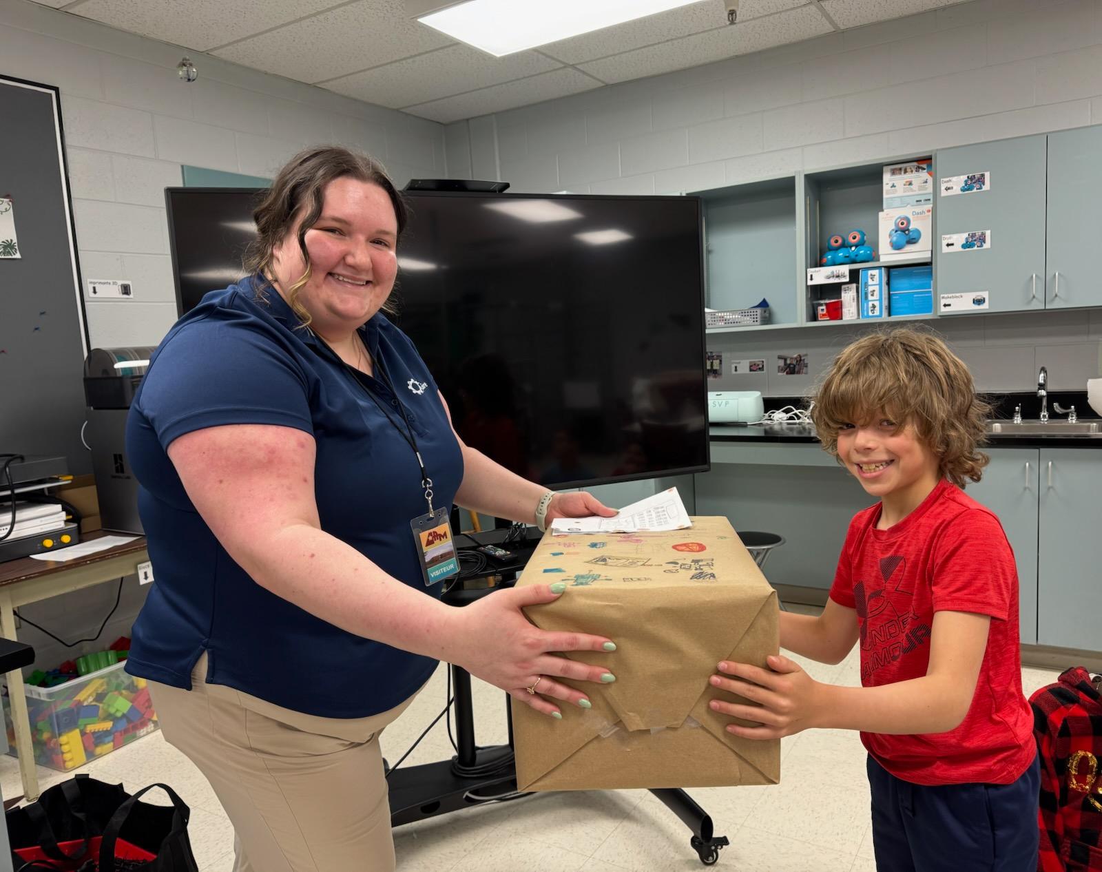 A student from École Anna-Malenfant hands Lianne a box with the assistive technology inside.