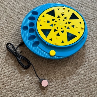 A raindrop switch plugged into a circular device that has multiple cutouts for holding paint and a piece that spins to hold a canvas