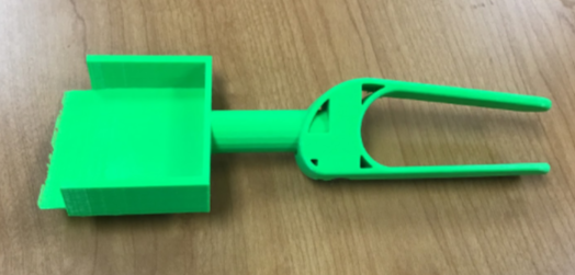 A green the 3D printed assistive scoop consisting of a handle that fits around the palm and a rectangular scoop.