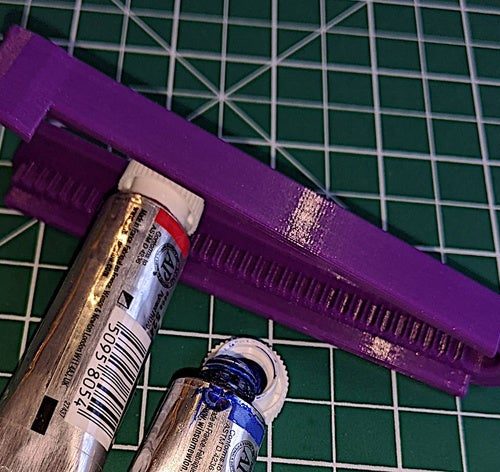 Picture of a purple 3d printed assistive paint tube opener being used to open a tube of paint.