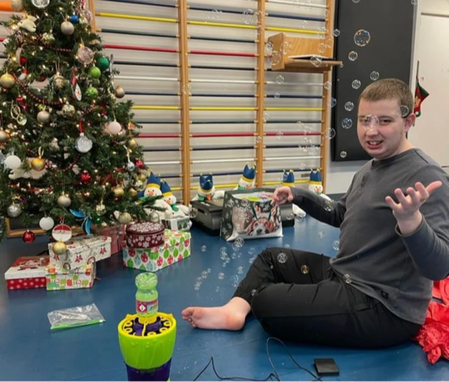 A user using a switch-adapted toy beside a Christmas tree.