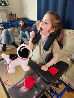 Briar in her wheelchair with a tray and her switch-adapted toy.