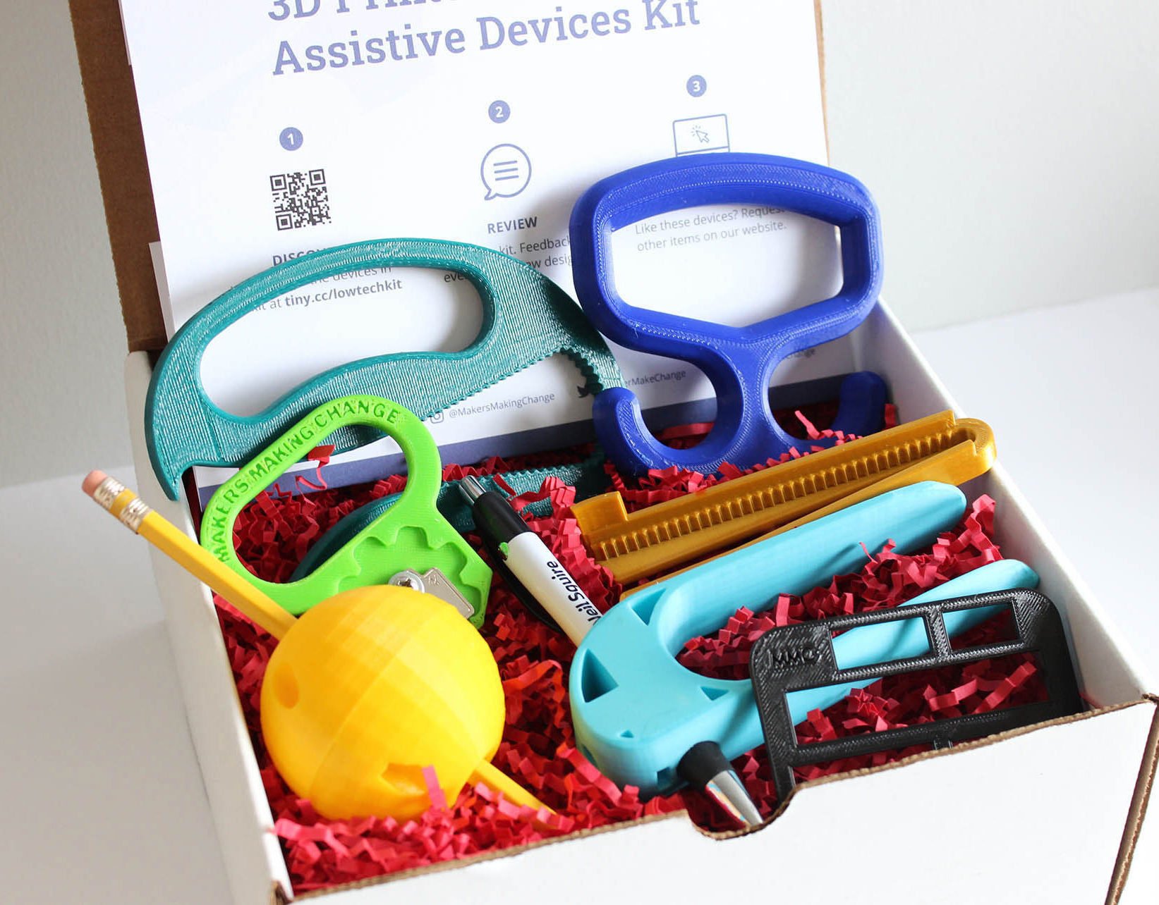 Nine 3d printed low-tech assistive devices in a white box.