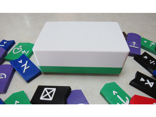 A green and white rectangular enclosure of the voice-it assistive device. Around it a dozen 3d printed bliss tactile symbols.