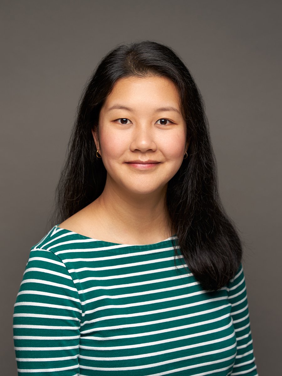 A woman with long black hair and striped green shirt against a grey background.