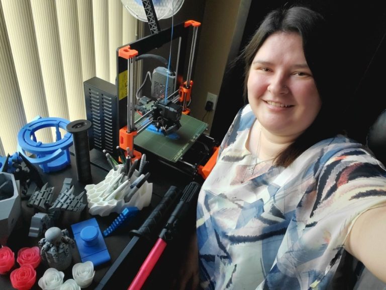Olivia, volunteer, smiling while standing beside a 3D printer.