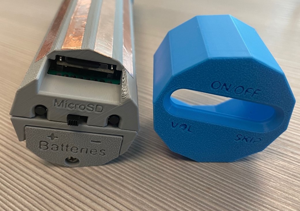 The end of the Musical Grasping Training Aid with the end cap removed, showing the power button, battery cover, and microSD slot.