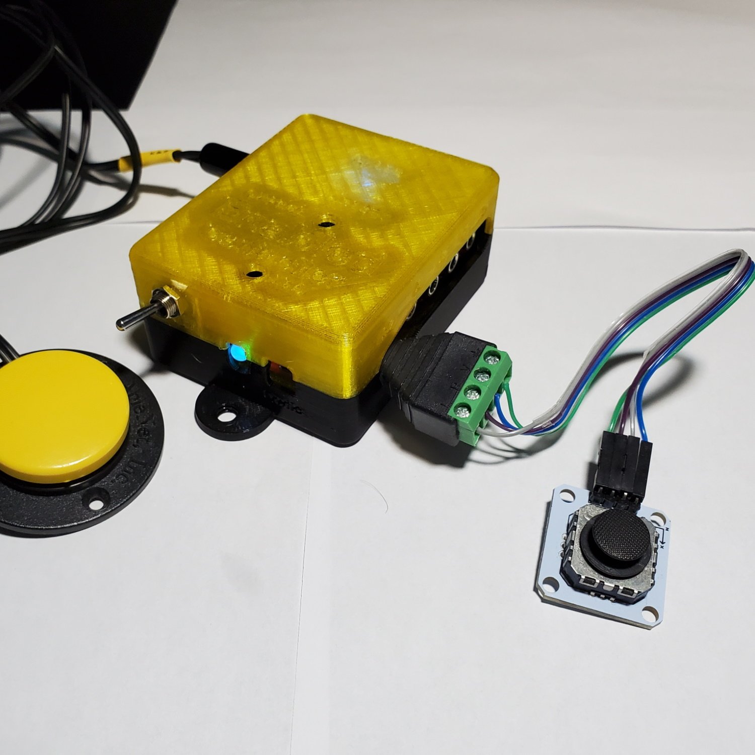 A rectangular enabled controller with a mono jack, joystik, and accessible switch plugged in.