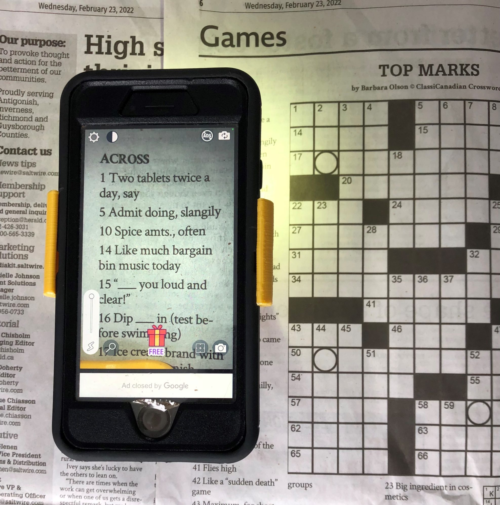 A phone displaying a magnified view of crossword clues on a newspaper.