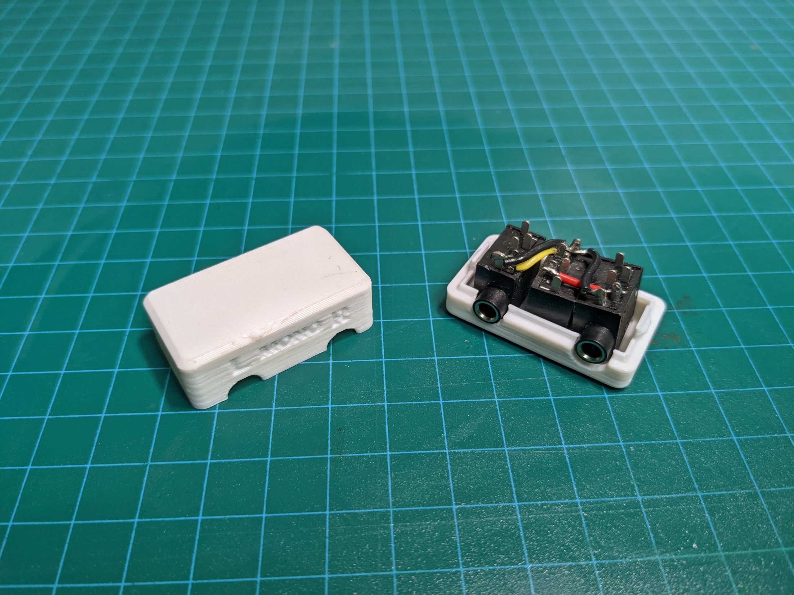 A uncovered mono-stereo switch adapter uncovered showing the internal electronics and lid.