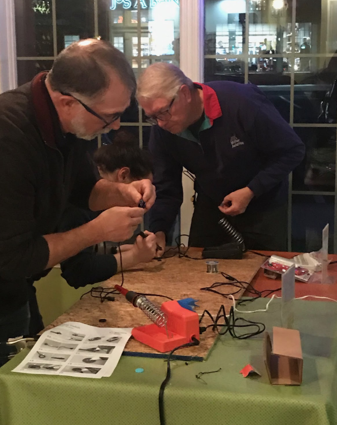 Makers at Winchester assembling an assistive device with a table that contains instructions, tools, and a soldering iron.