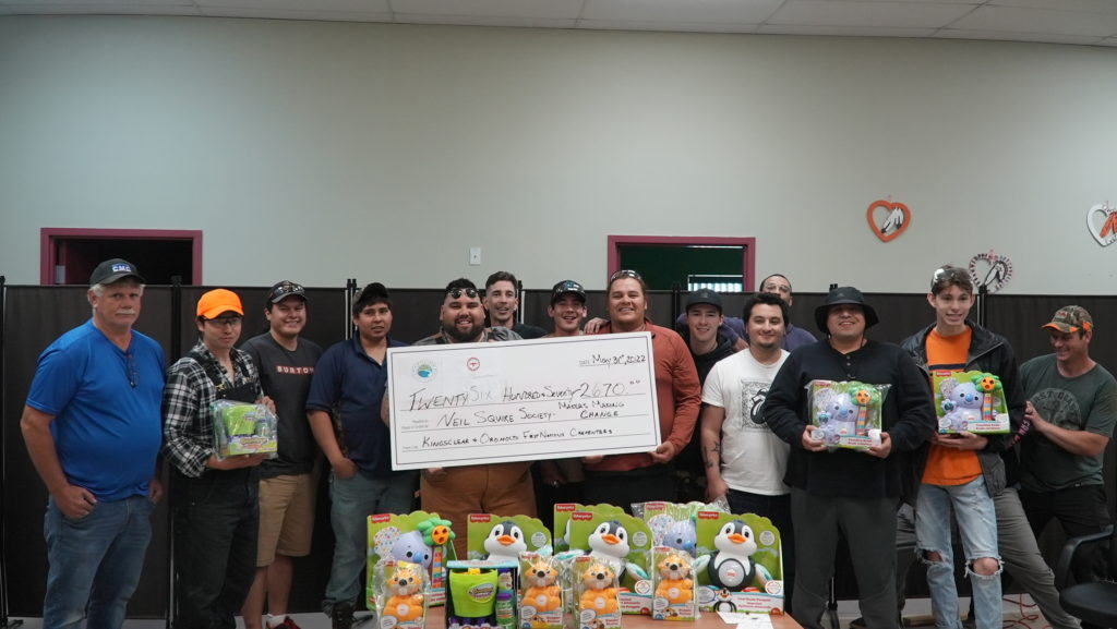 Participants at a build event holding adapted toys and a large cheque.