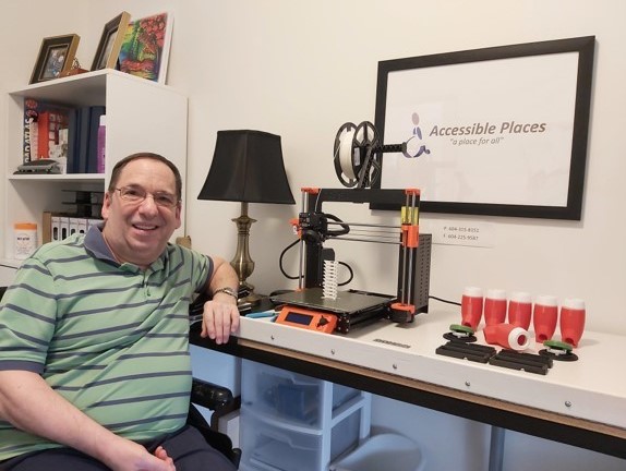 Alfred, a volunteer maker, smiling beside his 3D printer and assistive tech parts.