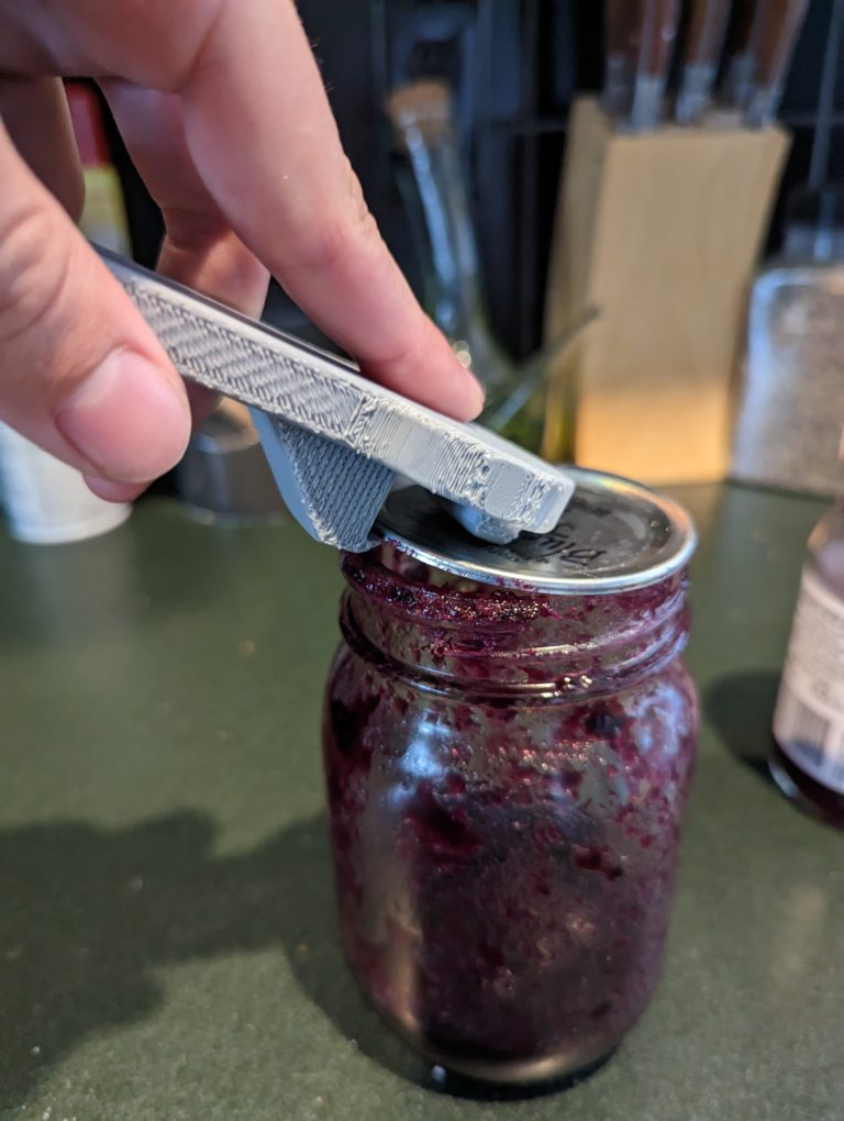 A grey jar lid opener being used to open a jar lid.