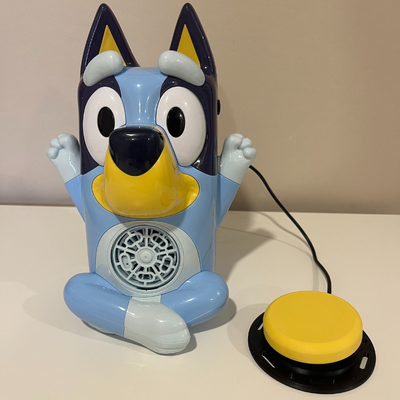 Bluey toy with a bubble fan in the middle of his stomach with a yellow assistive switch plugged into a jack in the back of the toy.