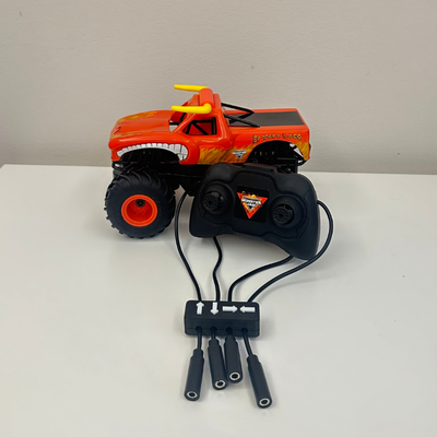 Orange remote control monster truck with a black switch adapted remote control with four mono cables coming out of it, each labeled with arrows.