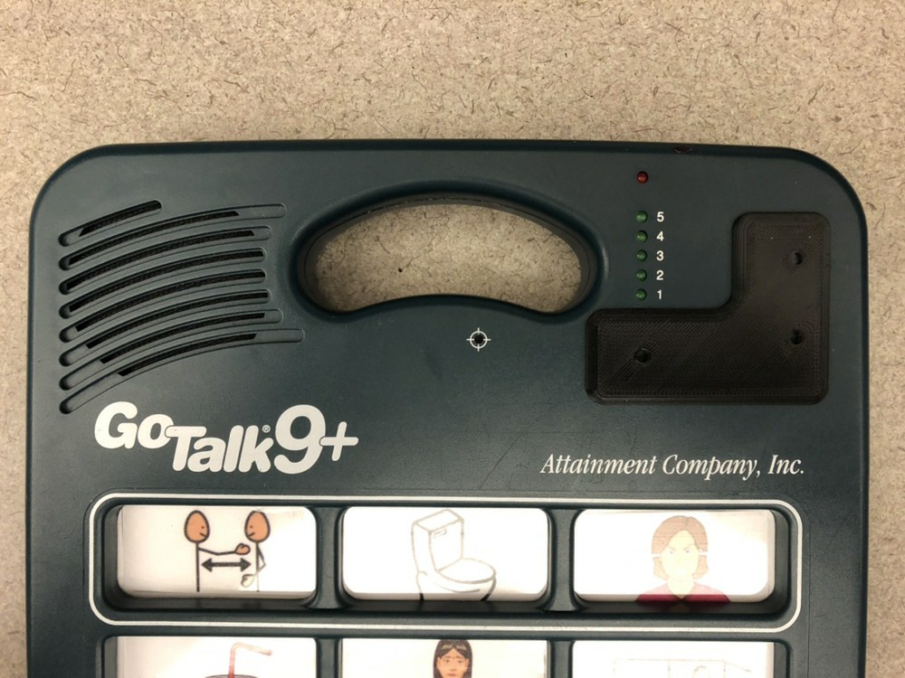 Picture of a Go Talk 9+ AAC device with a black 3D printed guard to limit access to the volume control and change level buttons in the upper right corner of the device.