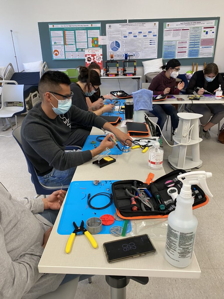 Volunteers soldering and building assistive tech.