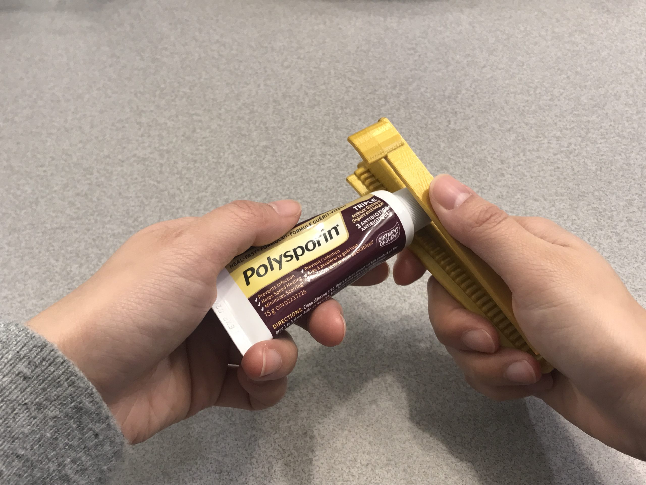 A hand opening a polysporin tube with the tube opener