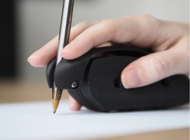 Hand on top of the DRAG black assistive writing aid.