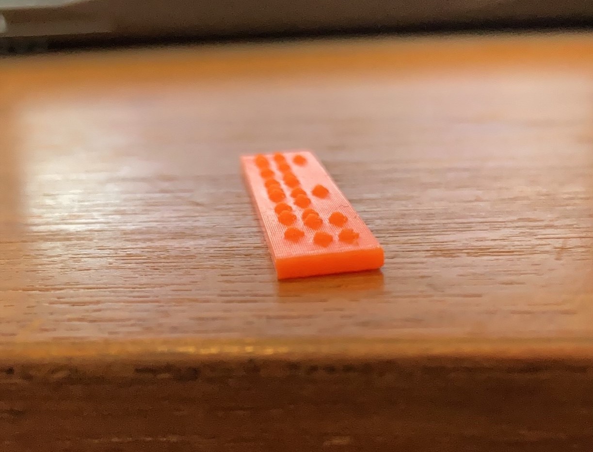 An orange 3d print rectangle with braille on a table.