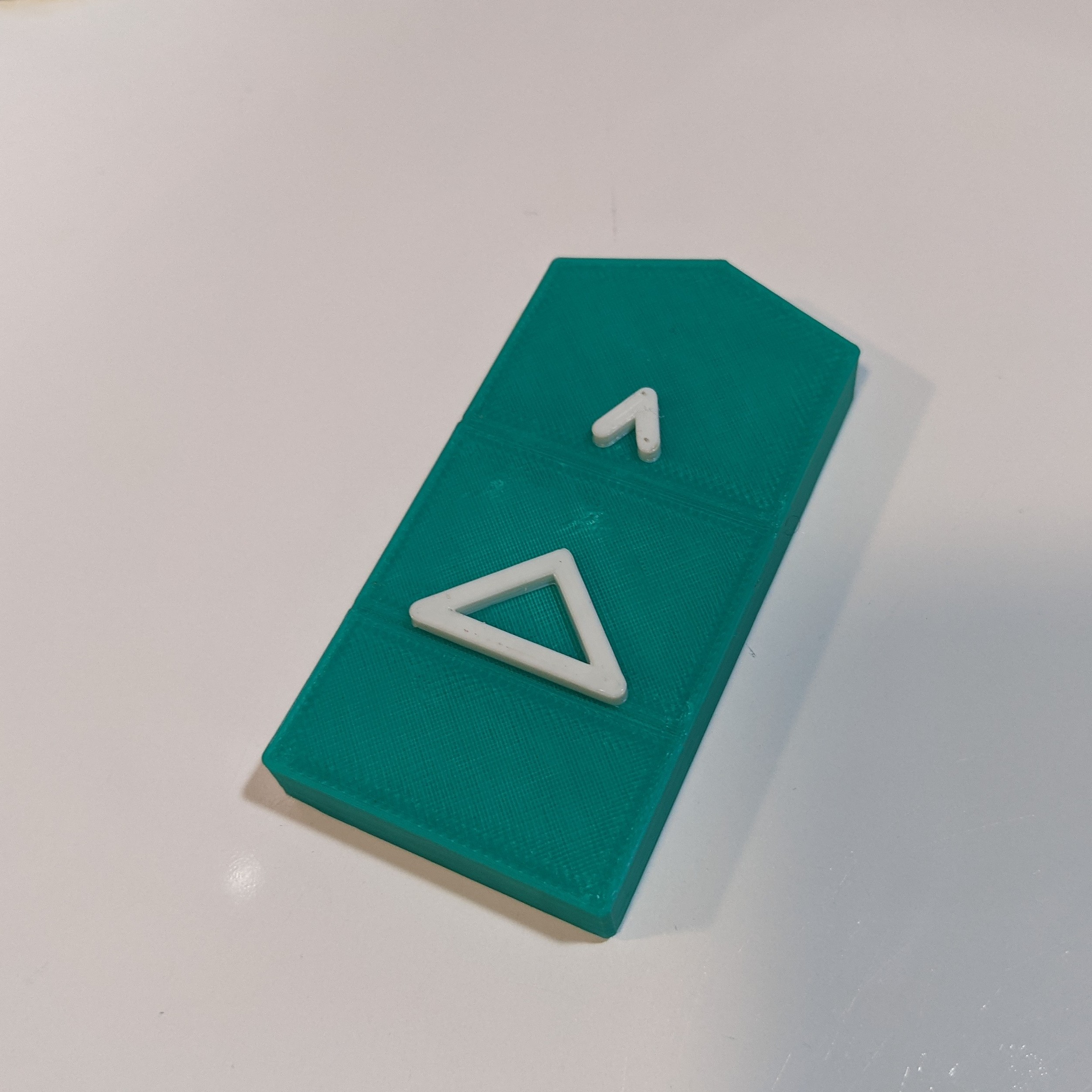 A green 3d printed bliss symbol for the word 'make'. The base is in green and the symbol is in white.