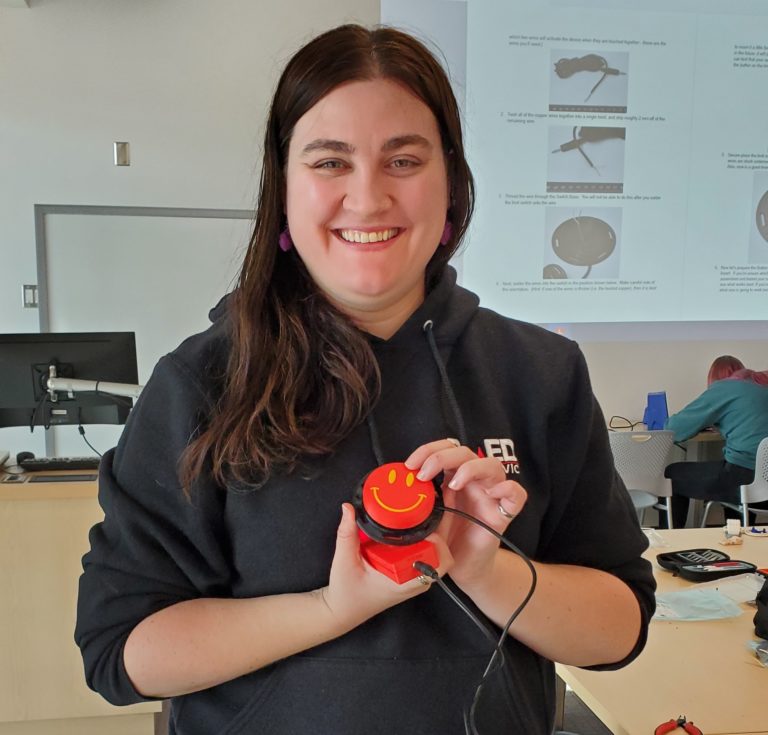 A UVIC student holding up a red smiley-face Interact Switch.