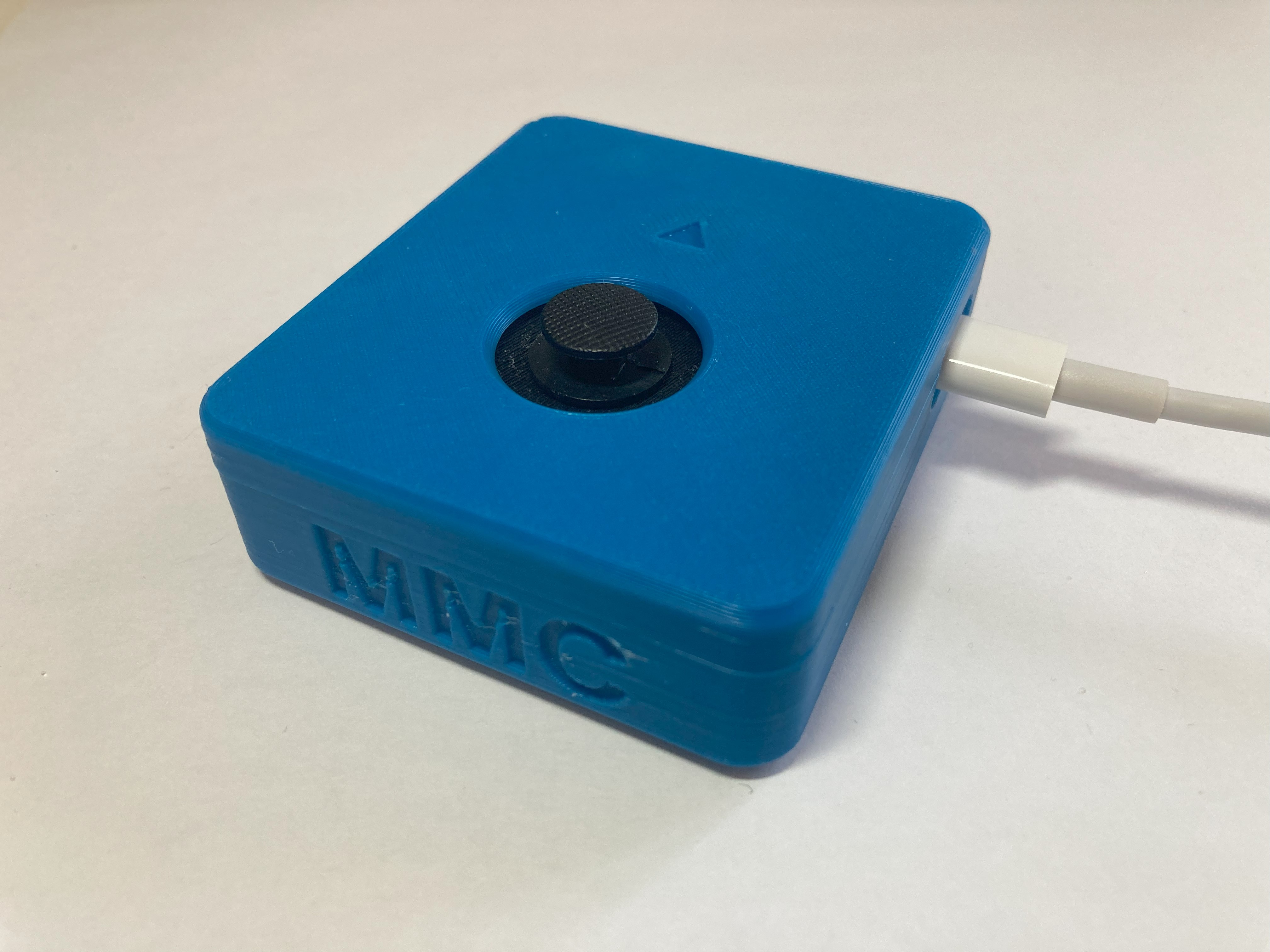 Light blue Birch Sliding USB Joystick on a white background. It is a rectangular shape with a black circle on top, and a smaller elevated black circle that is the joystick topper. There is a white USB-C cable plugged into the side.