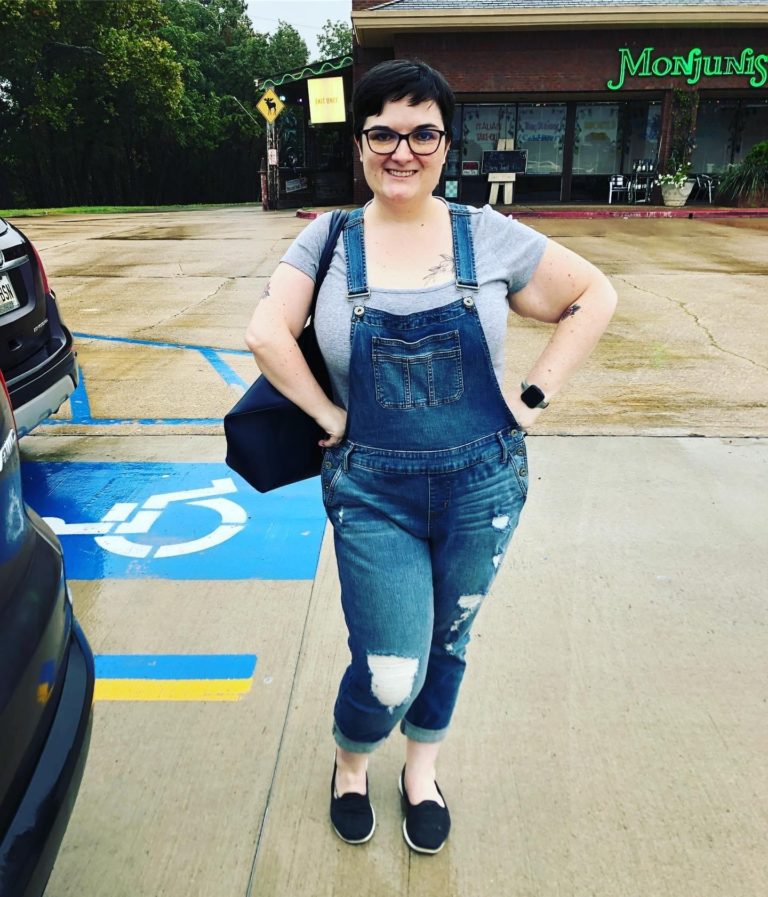 Ashley, a user, pictured wearing overalls in front of a store.