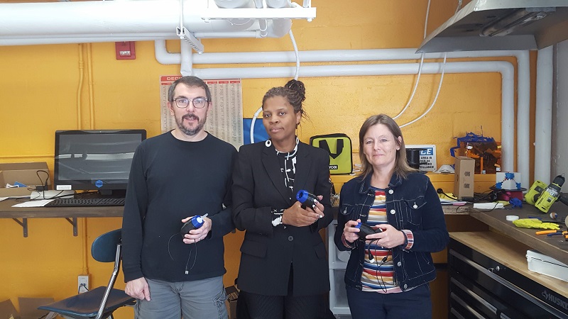 Three volunteers holding their built assistive devices at the GW Innovation Center.